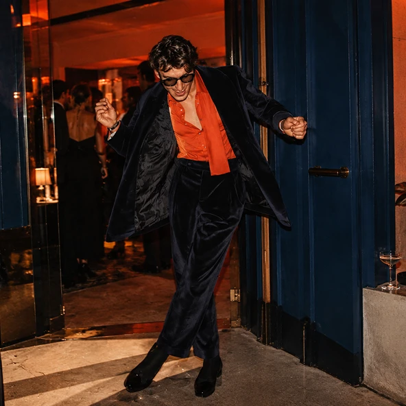 A man in a velvet suit dancing out of a restaurant doorway